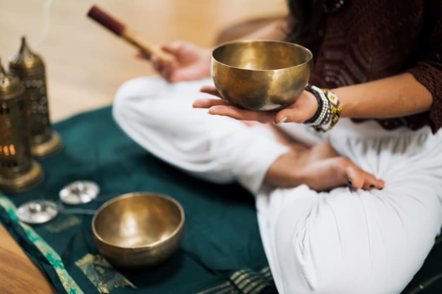 personne en tailleur avec un bol tibétain pendant une séance de méditation